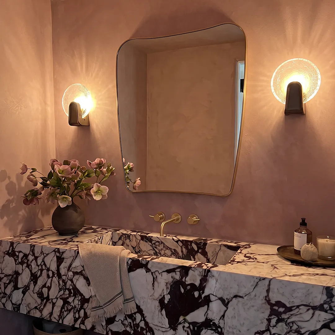Round textured glass wall sconce beside a bathroom mirror, modern brass wall light