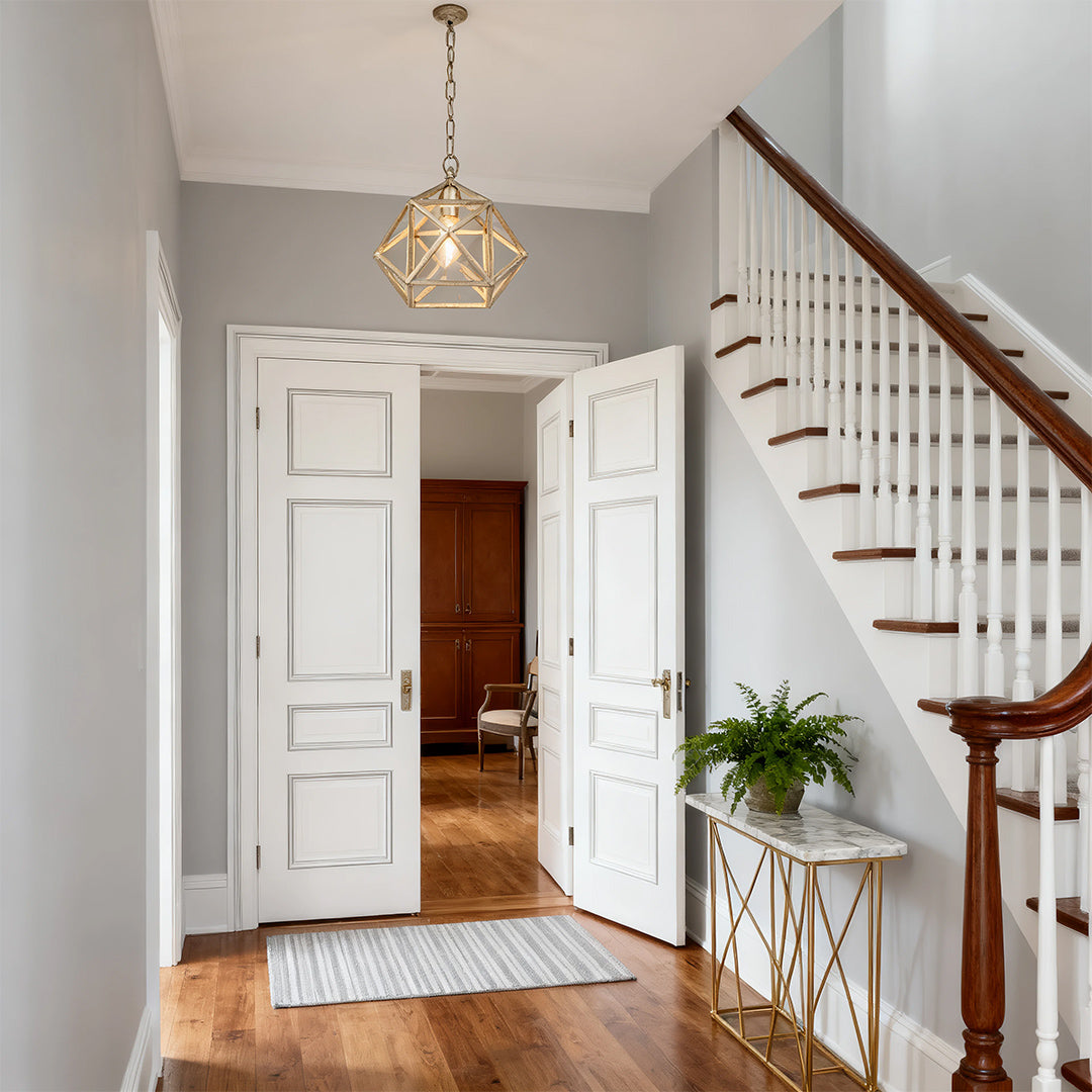 Gold geometric pendant light above a marble console in a white hallway staircase