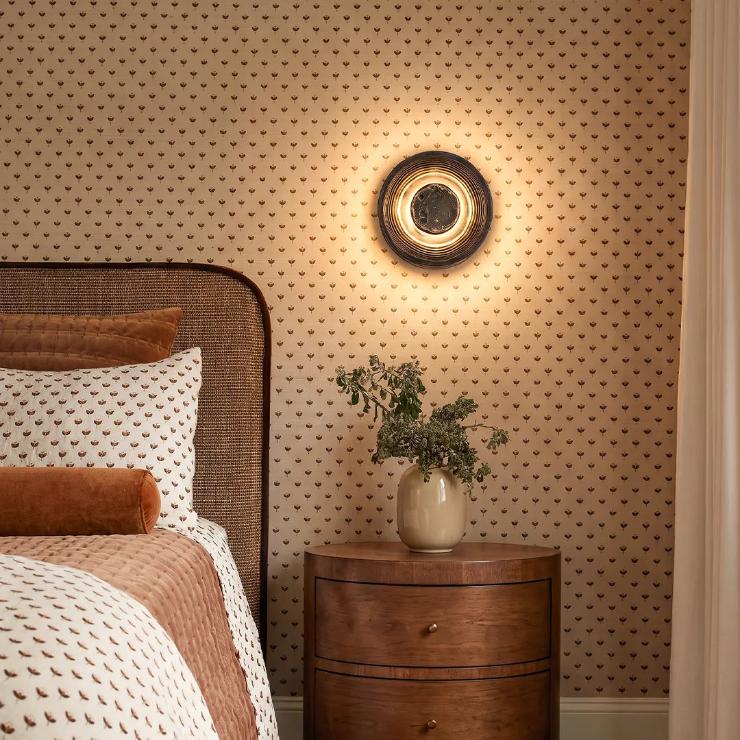 Niva round LED wall sconce mounted beside a bedroom nightstand as ambient accent lighting