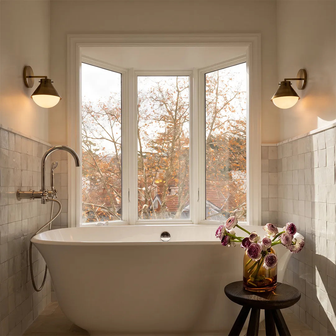 Gunmetal gray metal wall sconce mounted beside a bathtub with natural window light