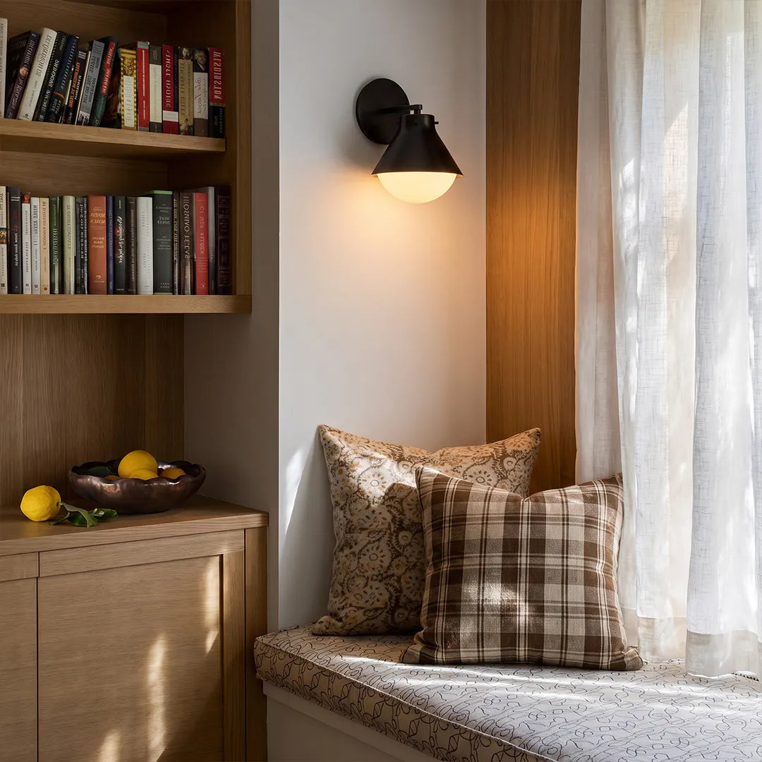 Metal and glass wall sconce in dark finish illuminating a reading nook corner