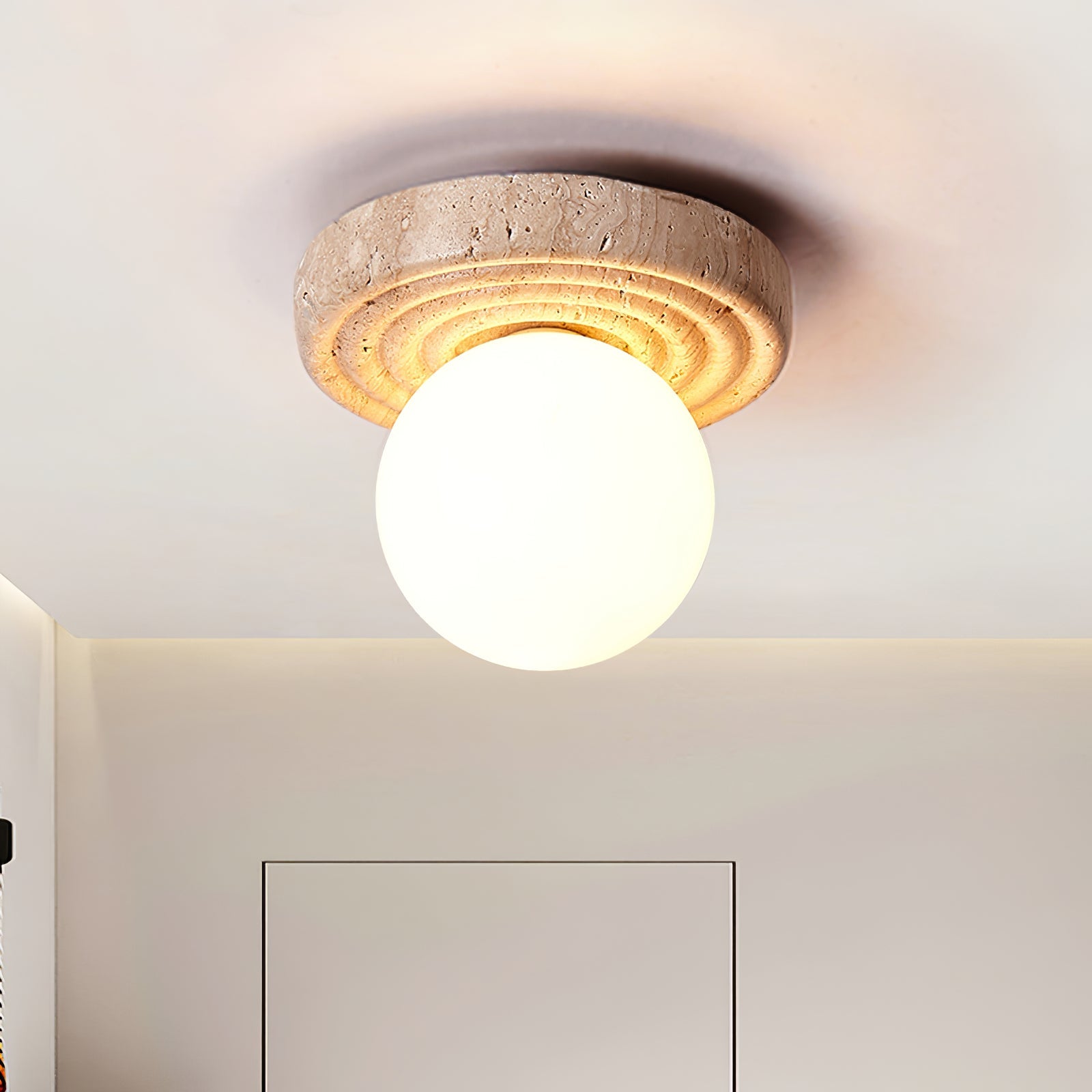 Emika travertine ceiling light switched on, casting soft diffused light in a minimal interior
