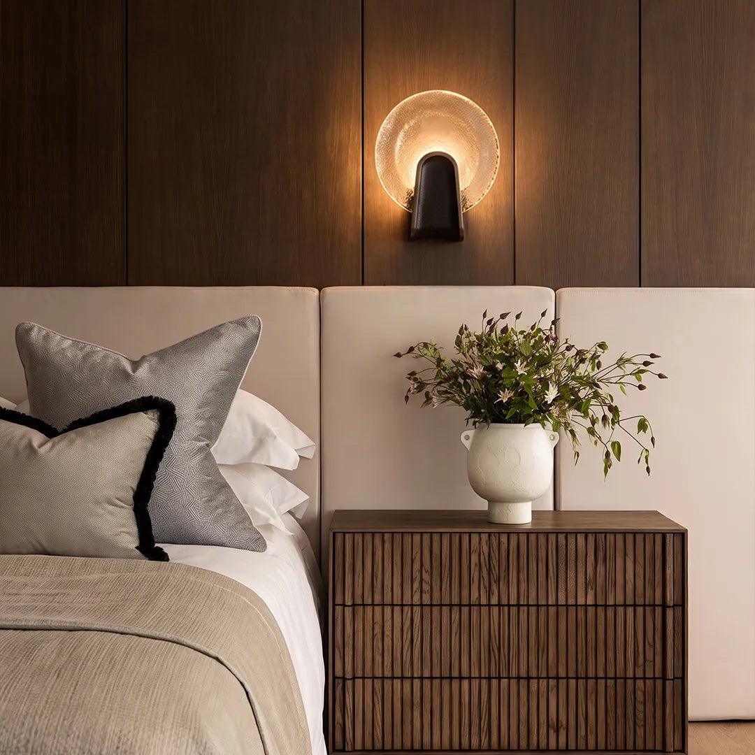 Black smoked glass round wall sconce above a bedside table in a modern bedroom interior