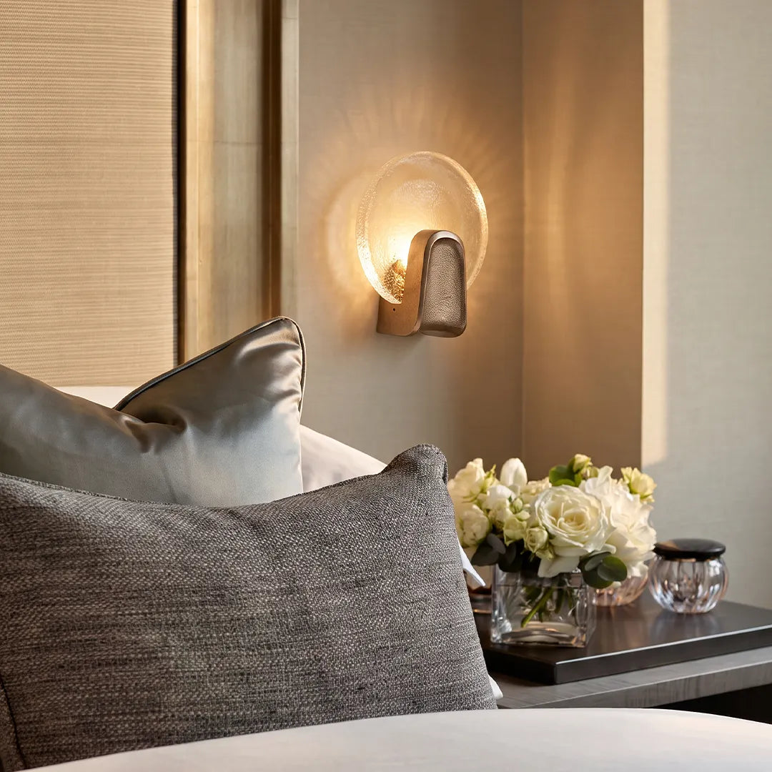 Round textured glass wall sconce at a bedside, warm modern brass wall light