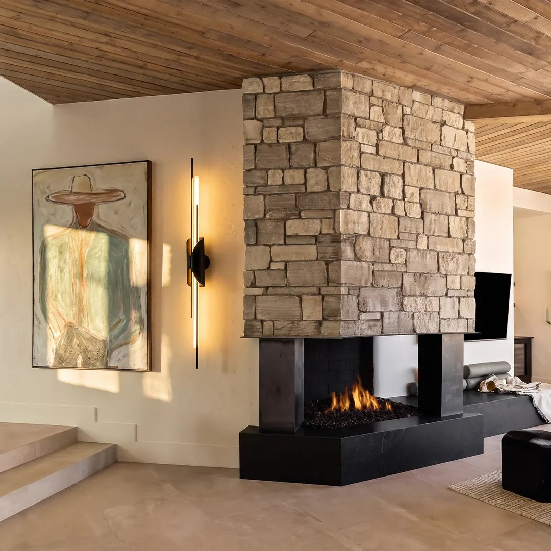 Linear brass wall sconce mounted beside a stone fireplace in a contemporary interior