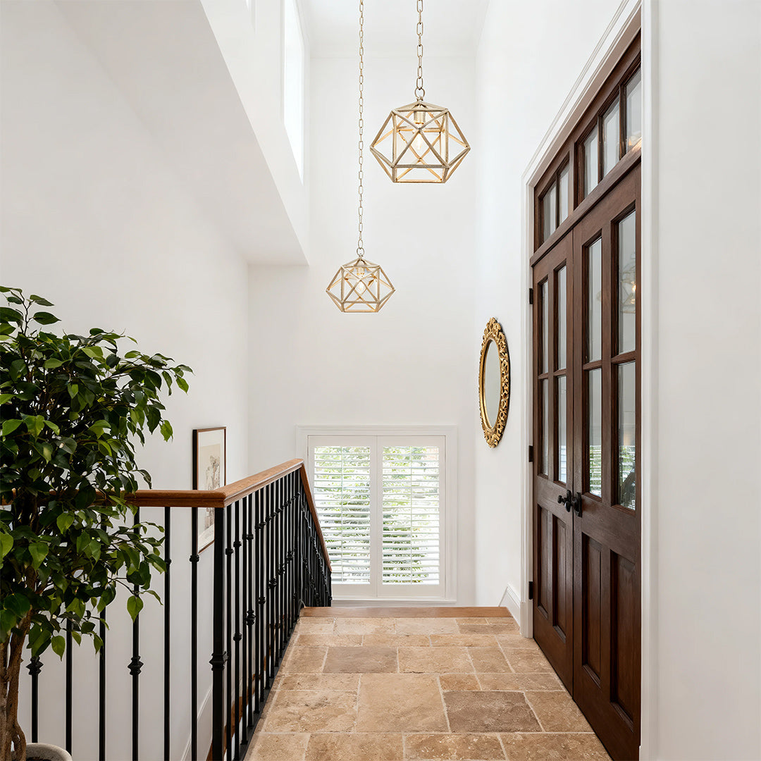 Gold open-cage geometric pendant light in a double-height entryway with wrought iron staircase