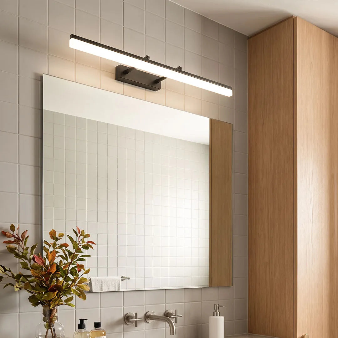 Gold vanity light bar on white tile bathroom wall above mirror