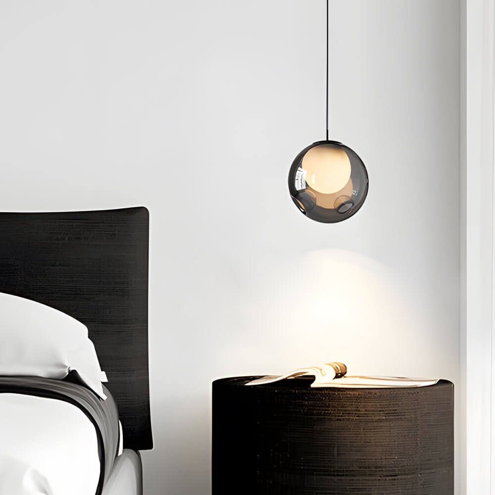 Minimalist smoked glass globe pendant light above a nightstand in a contemporary bedroom
