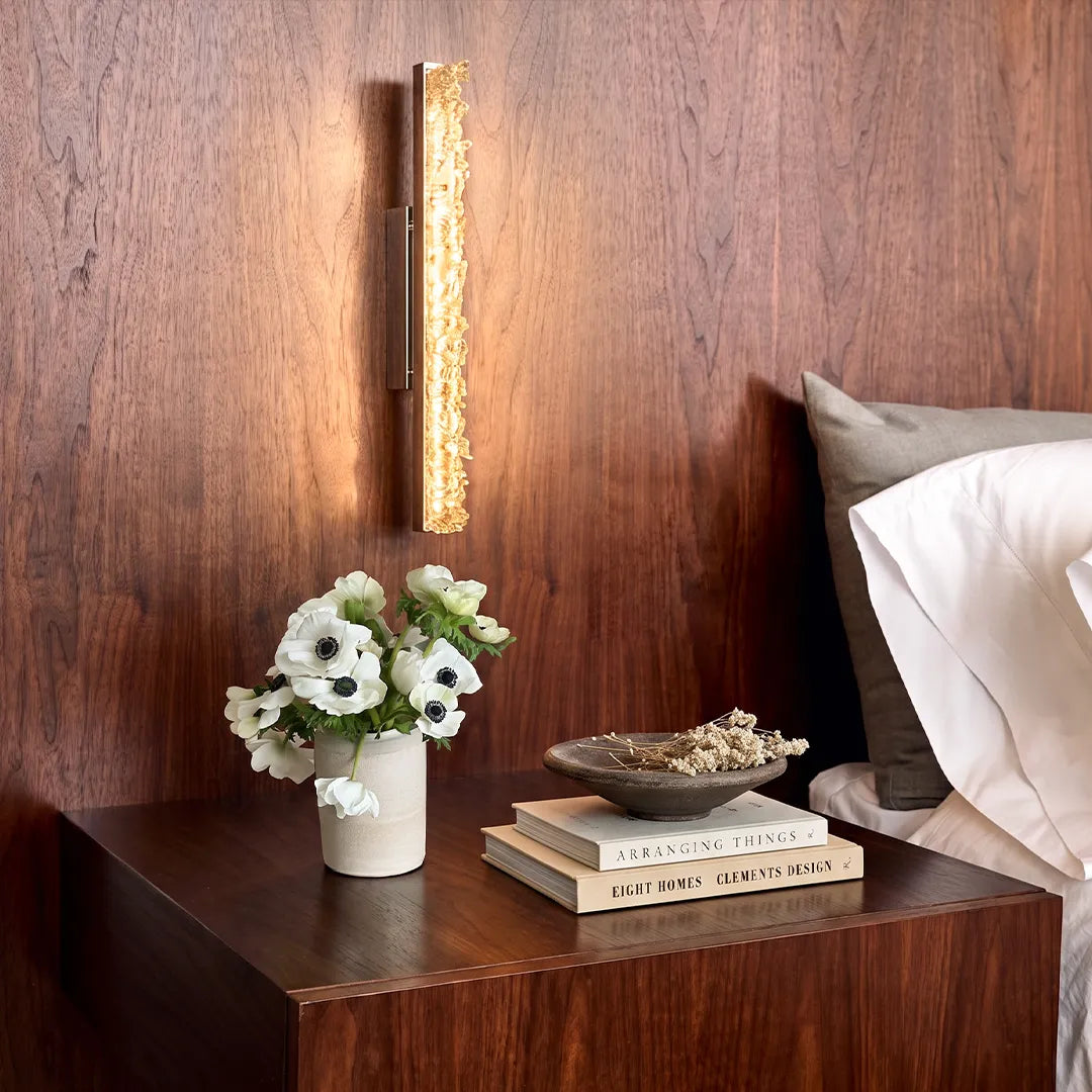 Niva crystal wall sconce mounted bedside on a wood-paneled wall in a contemporary bedroom