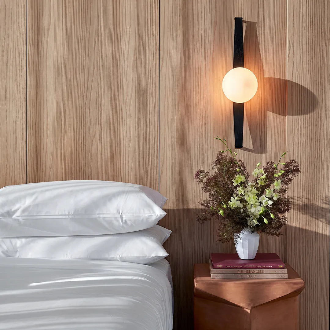 Niva globe wall sconce on a wood panel feature wall beside a bed, warm glow