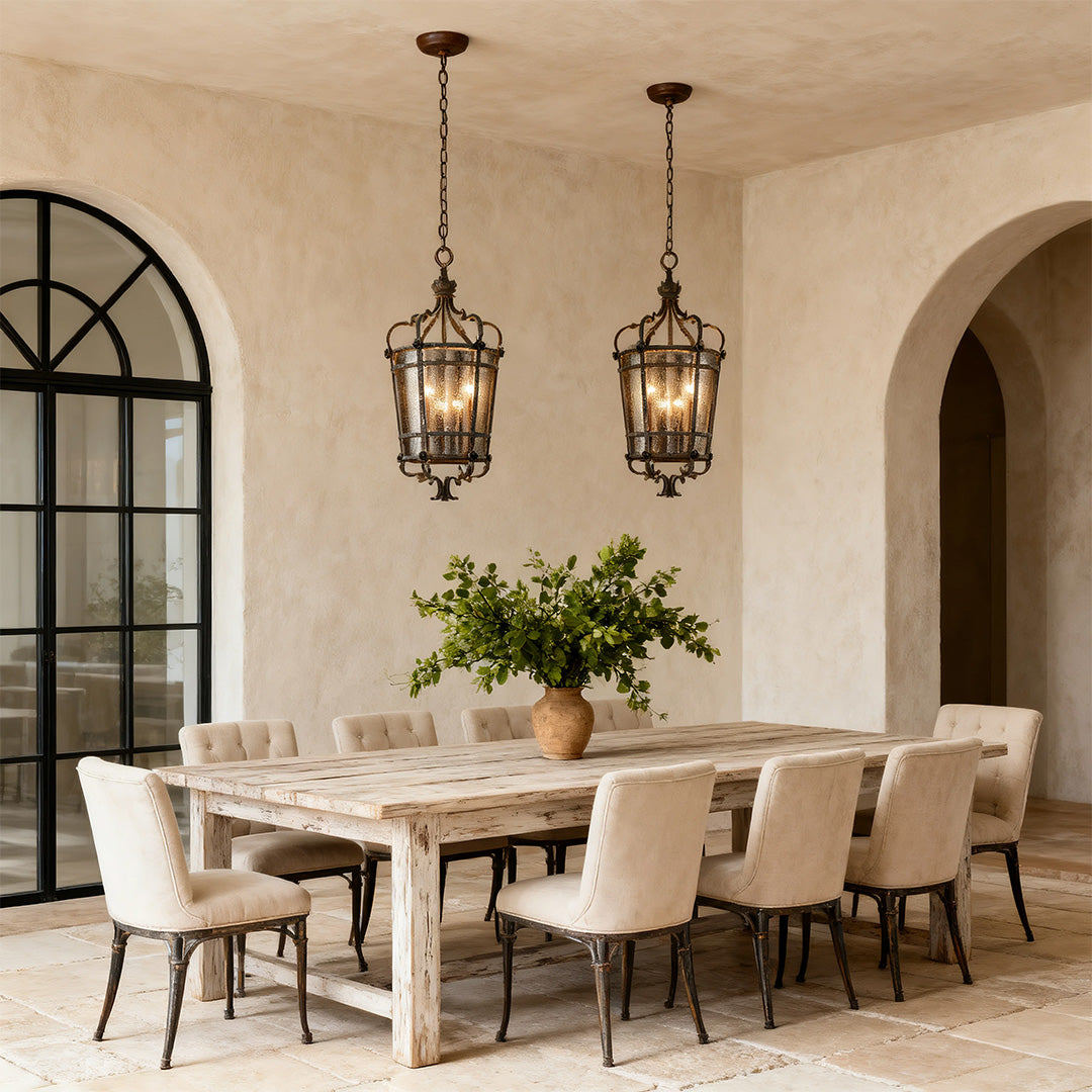 Pair of aged bronze iron lantern pendant lights above a rustic dining table in a Mediterranean-style interior