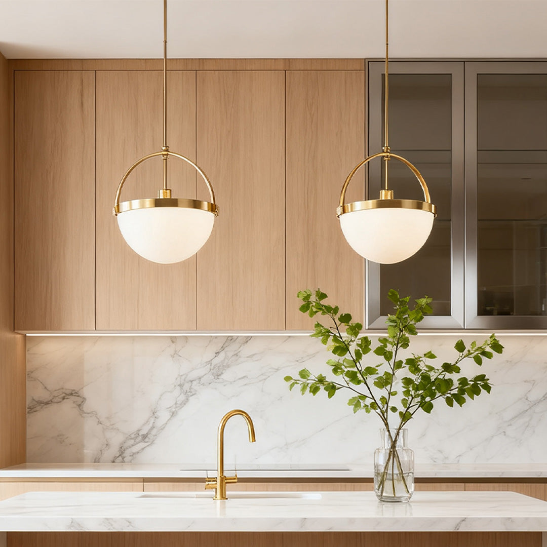 Pair of gold and white pendant lights above a kitchen island with marble backsplash and wood cabinets