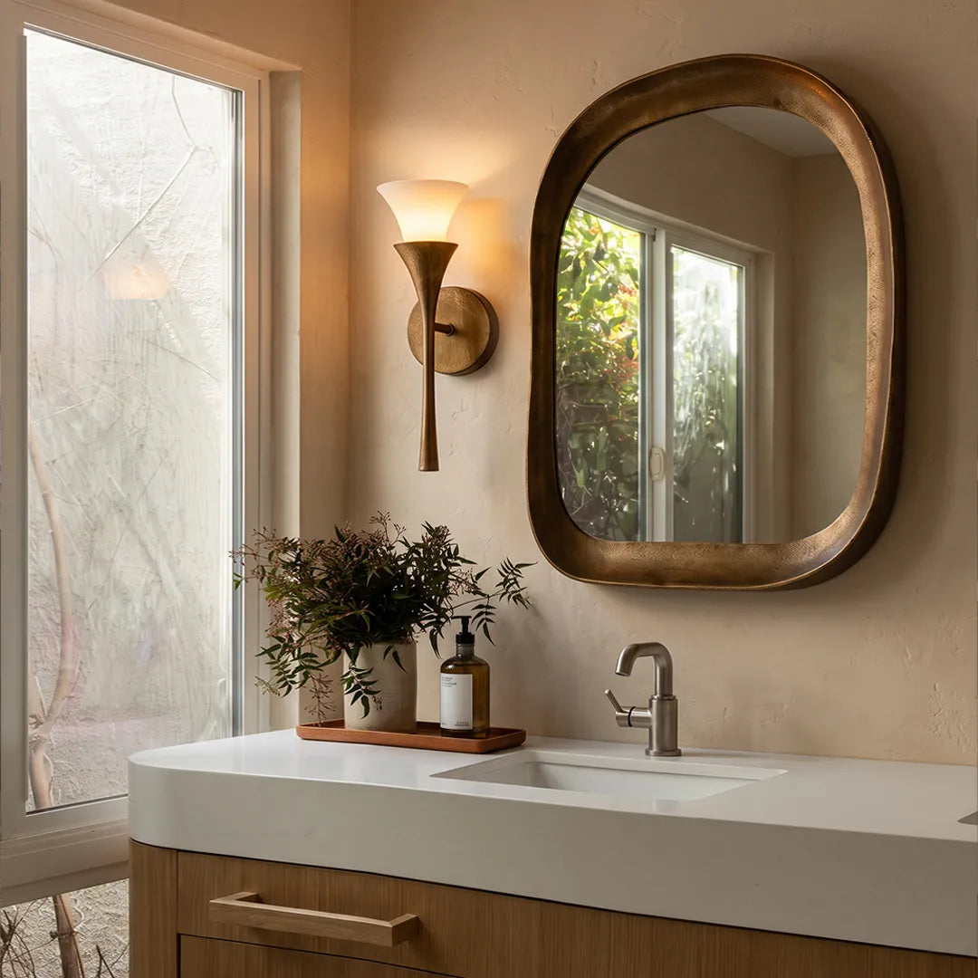 Niva antique brass wall sconce mounted beside a bathroom mirror