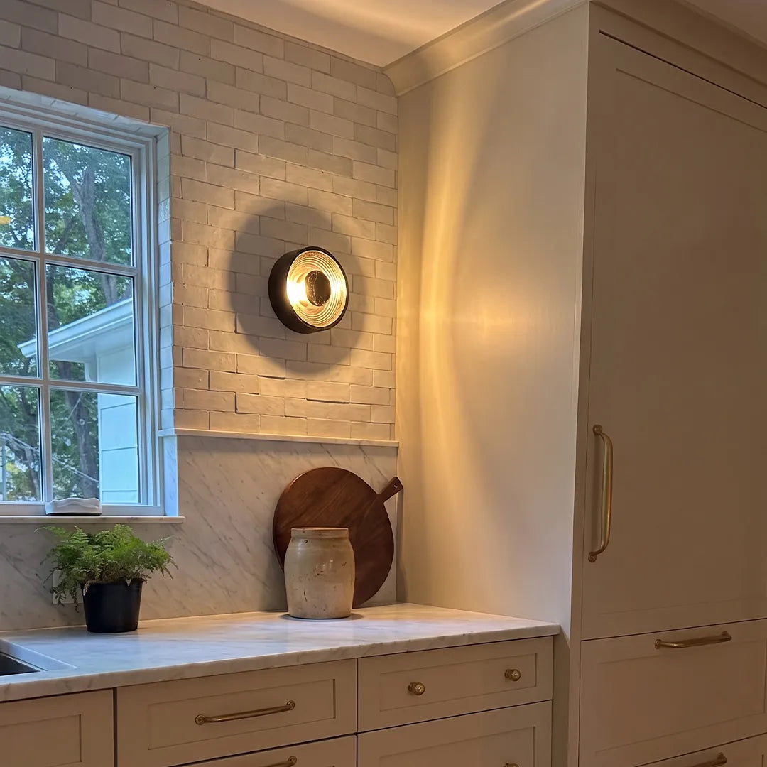 Niva round wall sconce beside a bathroom window, showing warm ambient light output