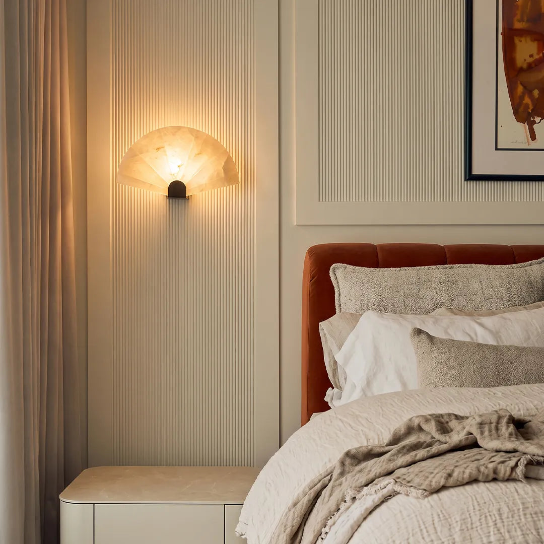 Scalloped marble wall sconce used as a bedside light, warm LED glow against a bedroom wall