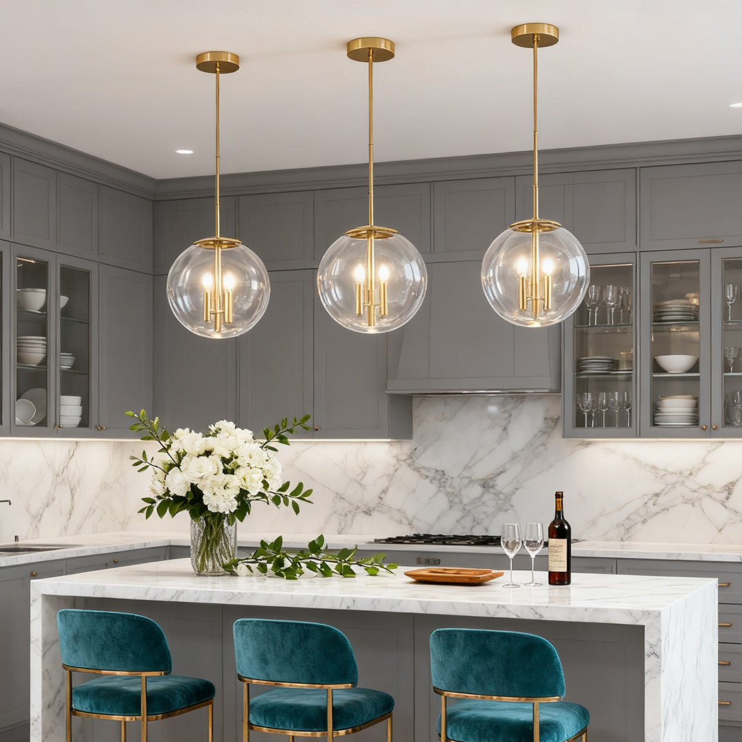 Trio of contemporary brass and clear globe pendant lights above a kitchen island